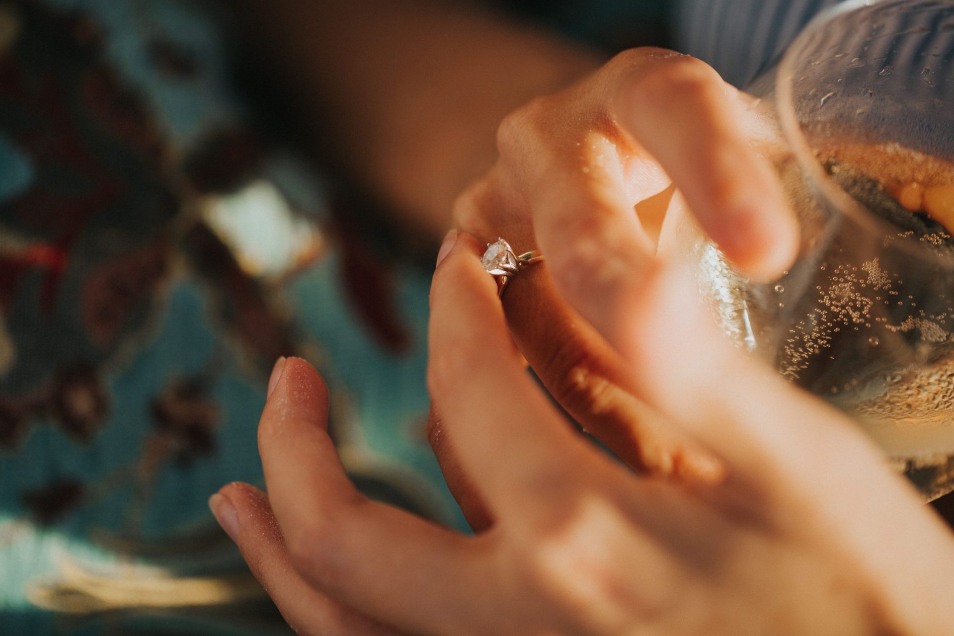 Close-up of two hands holding a glass. One hand holds a wedding ring.