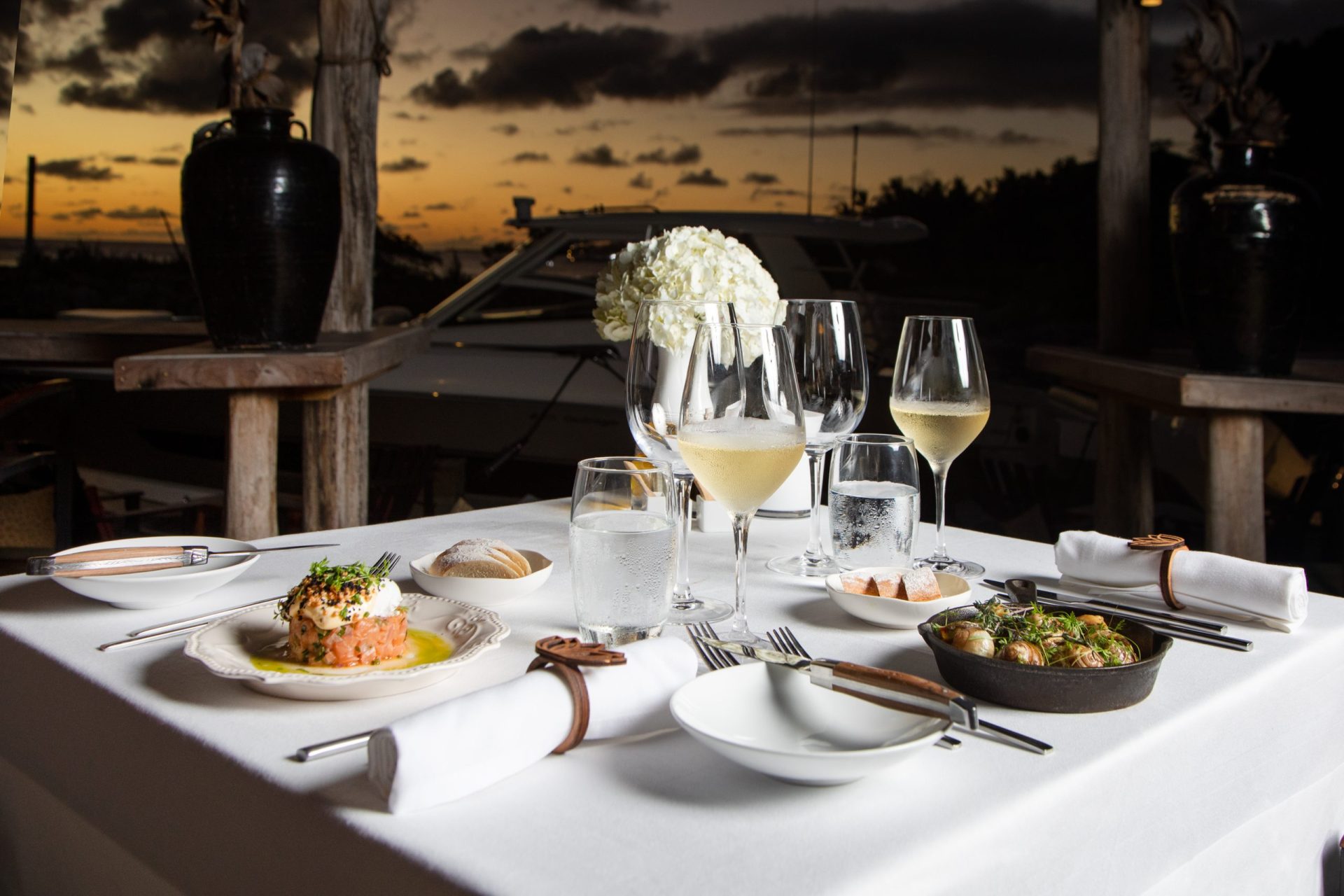 Table set with dishes and wine with in the background a yacht and a sunset