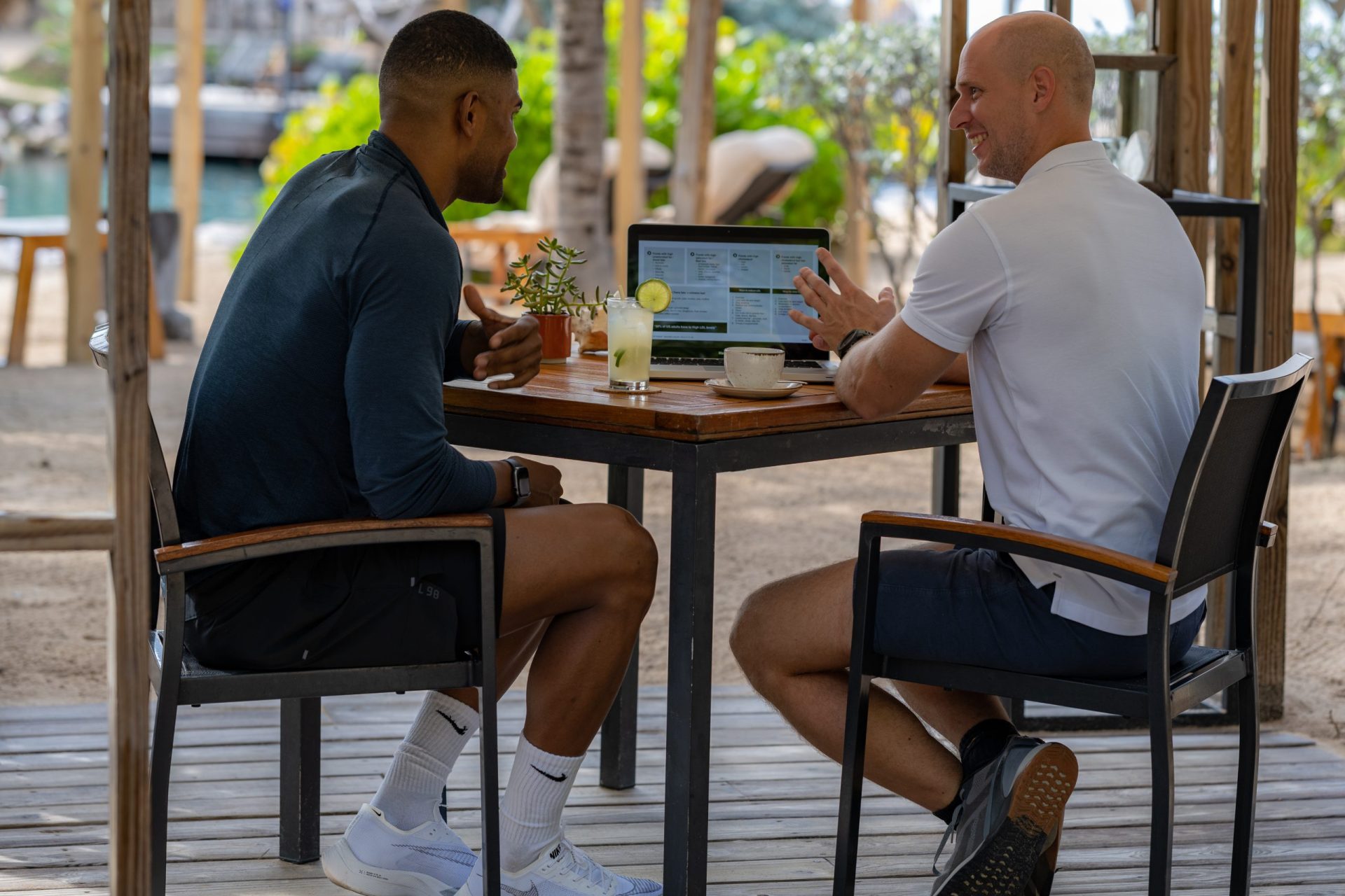 Two men in gym clothing having a drink at Baoase while watching a laptop