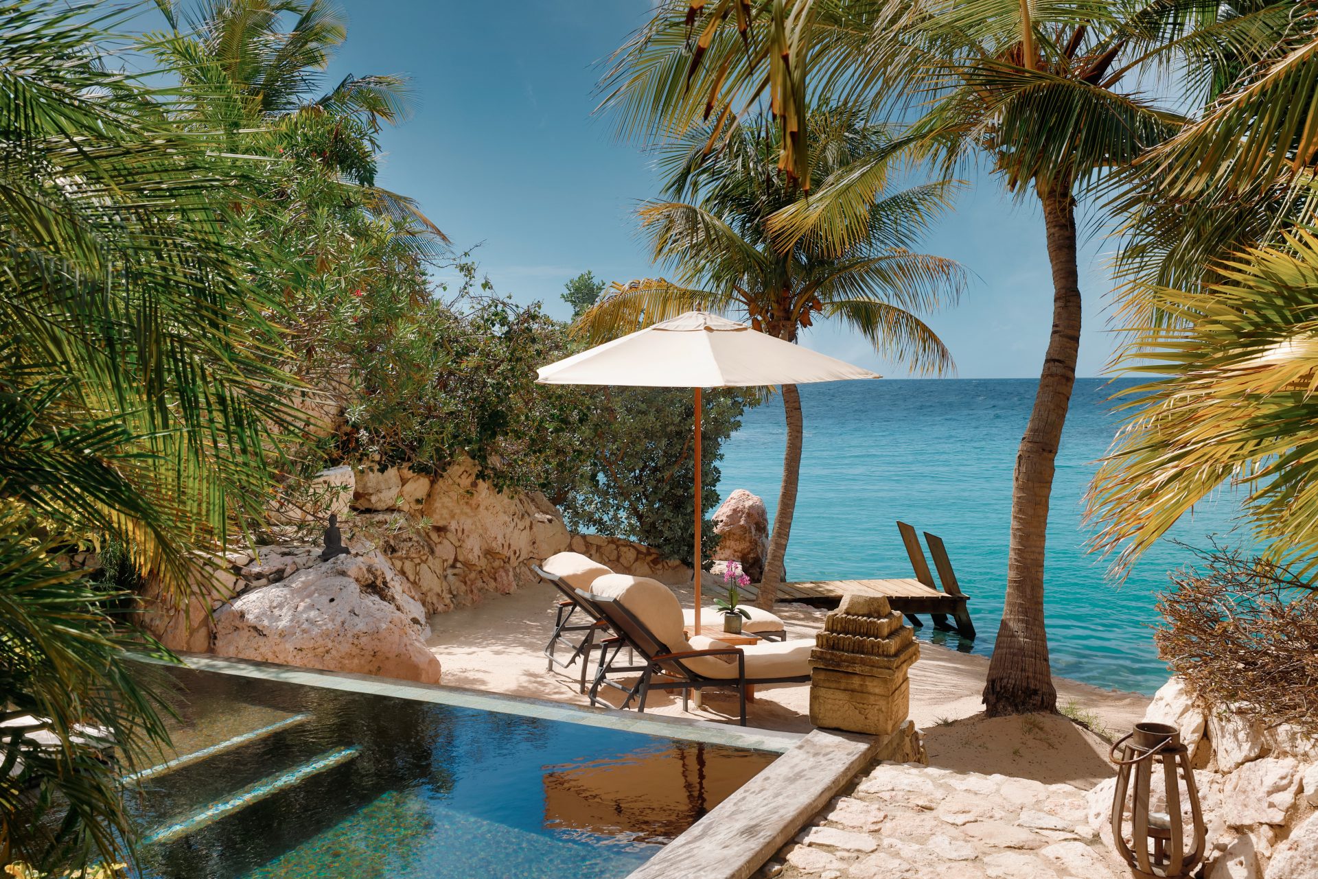 Corner of a pool next to a small private beach with entrance to the sea