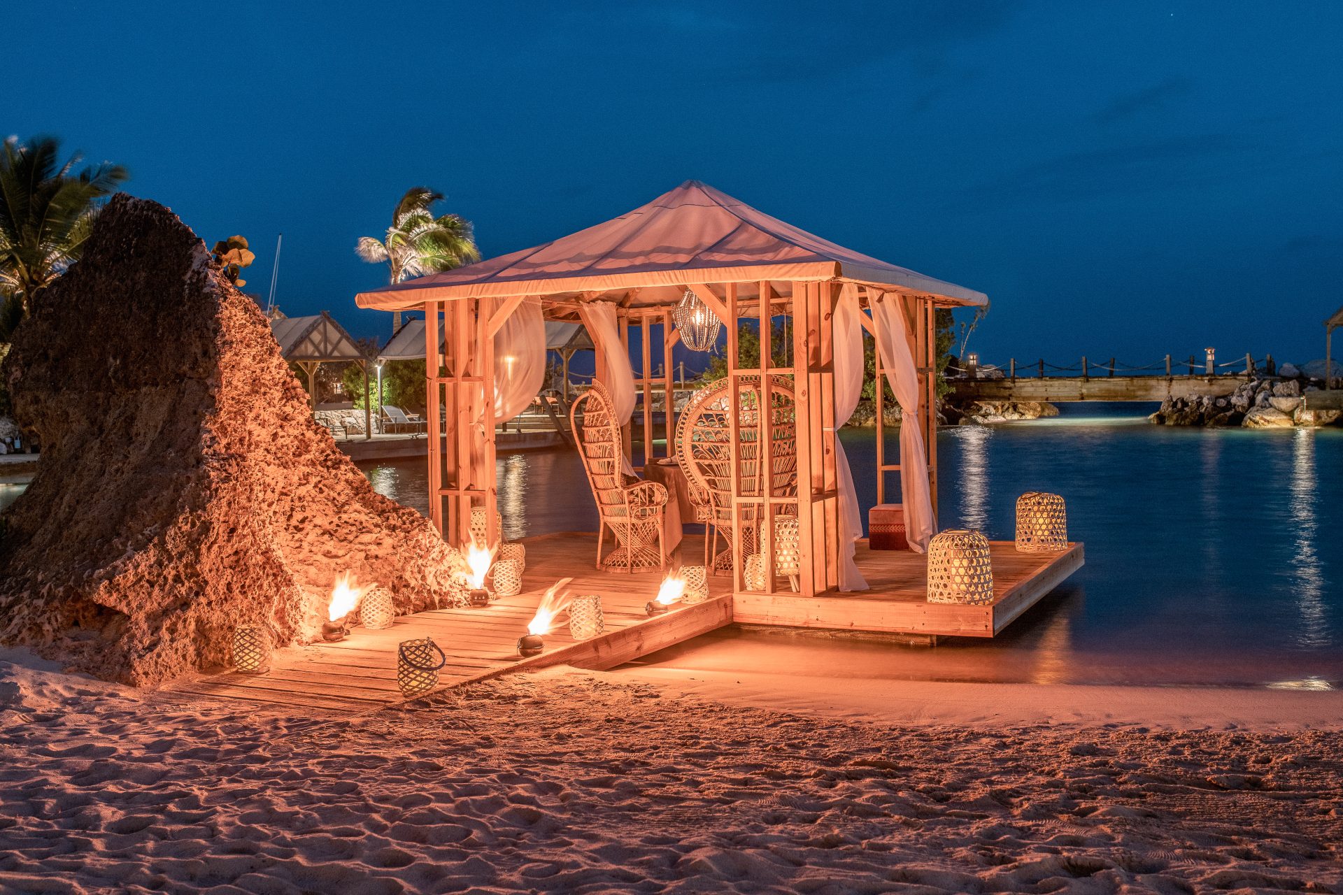 Romantic pier gazebo at Baoase Luxury Resort by night, illuminated with warm lights and candles along the water.
