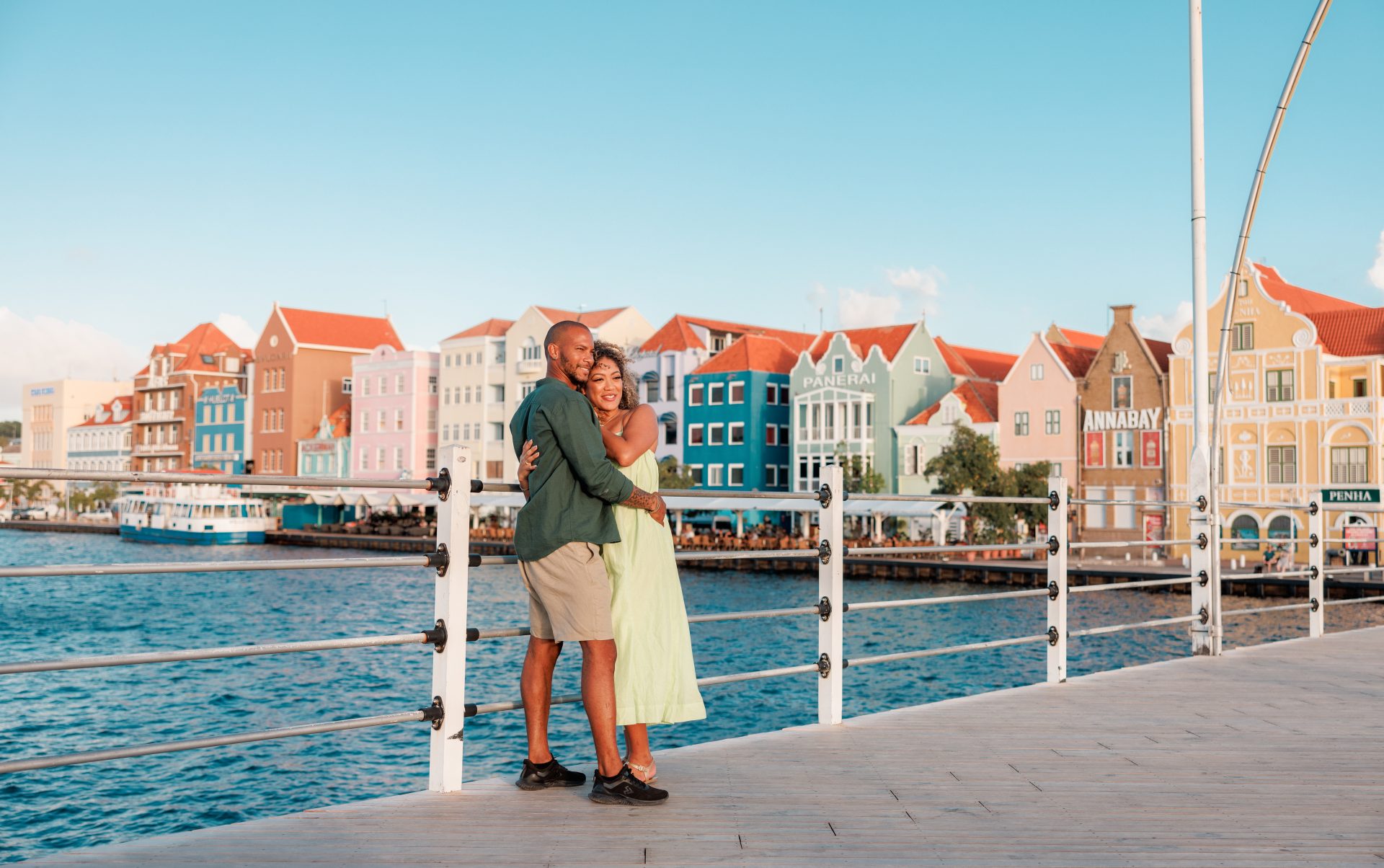 Couple standing along the waterfront in Willemstad with the colorful Handelskade buildings in the background.